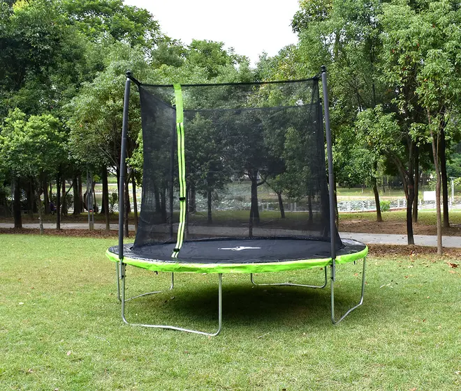 Rund udendørs trampolin med grøn kantpolstring, sikkerhedsnet og lynlåsåbning. Støttes af metalben, egnet til børn og voksne, placeret på græs i have.