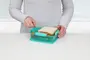 Rektangulær turkis madkasse med opdelte rum, vist med en sandwich og snacks. Sikker snaplukning. Fremstillet af holdbar plast, ideel til at holde mad adskilt.