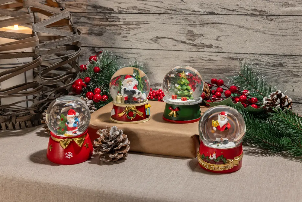 Fyra juliga snöglober med tomte, snögubbe och julgran, alla med röda och gröna baser, perfekta som dekoration eller present till julen.