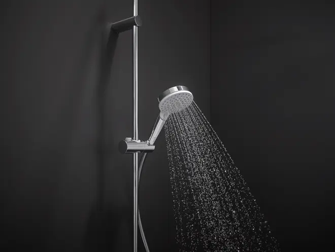 Modern handhållen dusch i krom med justerbart väggfäste, flexibel slang och flera munstycken, visas med vattenstråle i ett mörkt, stilrent badrum.
