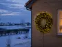 Varmhvid LED-julekrans monteret på en murstensvæg med tæt grønt løv, lysende lys og synlig ledning. - Billedet er skabt med AI