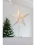 Oplyst hvid papirstjernelampe med fine udskæringer, monteret på en slank hvid fod. Perfekt til juledekoration, udsender varmt lys. Synlig ledning, moderne festligt design.