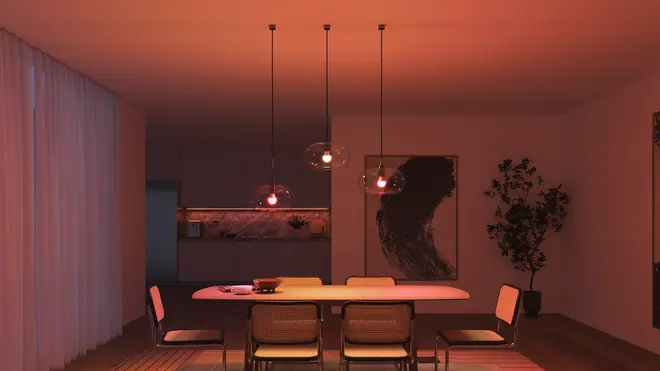 Moderne spisestue med seks stole med flet-ryg, rektangulært bord, tre pendellamper, abstrakt vægkunst, potteplante og blødt orange lys. Minimalistisk indretning med gardiner og tæppe.