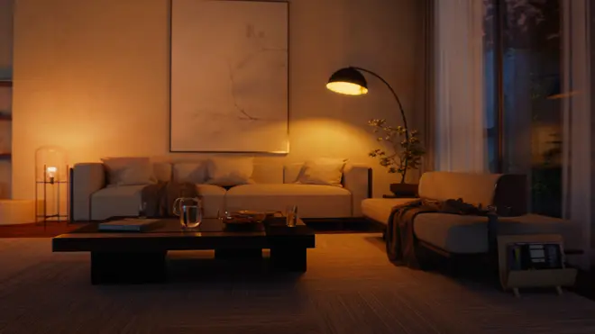 Moderne stue med beige sofaer, lavt sort sofabord, gulvlampe, abstrakt vægkunst og hyggelig belysning. Indeholder pyntepuder, plaid og glaskande på bordet.