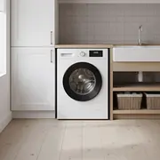 Moderne hvid frontbetjent vaskemaskine med digitalt display, placeret under træbordplade ved siden af høj skab. Minimalistisk bryggers med hylder, kurve og landlig vask. - Billedet er skabt med AI