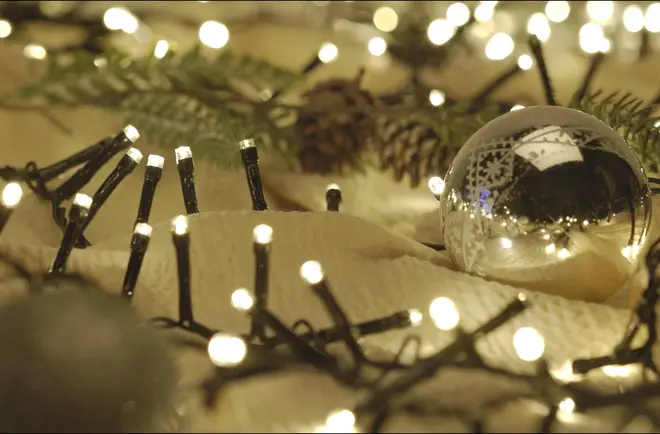 Varme hvide lyskæder flettet i granranker med en reflekterende glasjulekugle, som skaber en hyggelig festlig juledekoration.