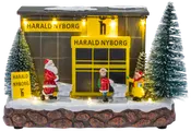 Oplyst miniature julebutik med sne, to grantræer, nissefigurer, indkøbsvogne og Harald Nyborg-skilte.