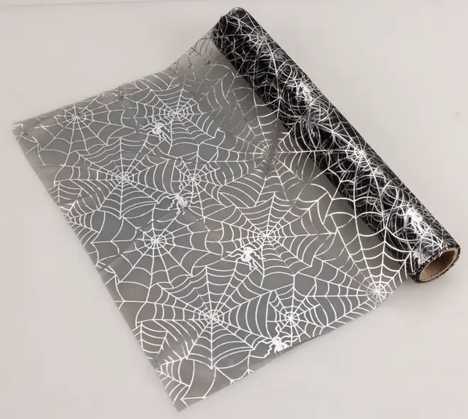 Transparent plastfilm med vita spindelnäts- och spindelmönster, perfekt för Halloween-dekorationer eller presentinslagning. Dekorativ, lätt och enkel att klippa till.