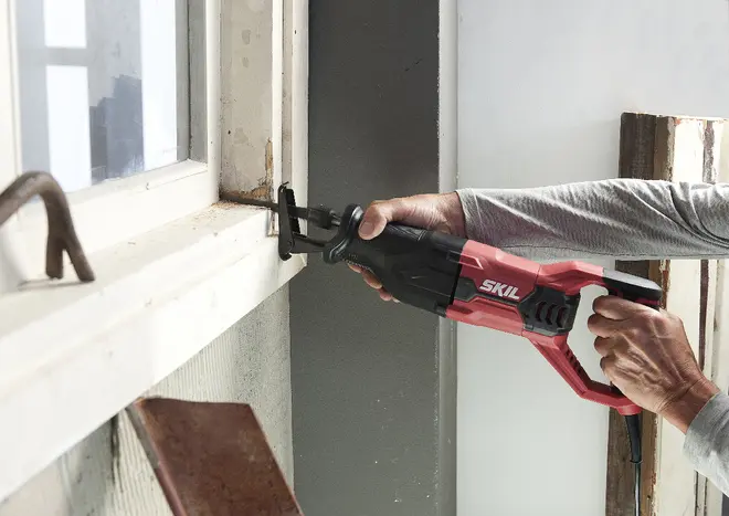 Röd och svart SKIL tigersåg med ergonomiskt handtag, används för att såga i ett fönsterkarm. Passar för rivning, renovering och träarbete.