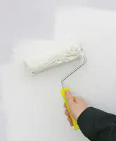 Målarroller med gult handtag används för att applicera vit färg på en vägg. Rollern har en mjuk yta för jämn täckning.