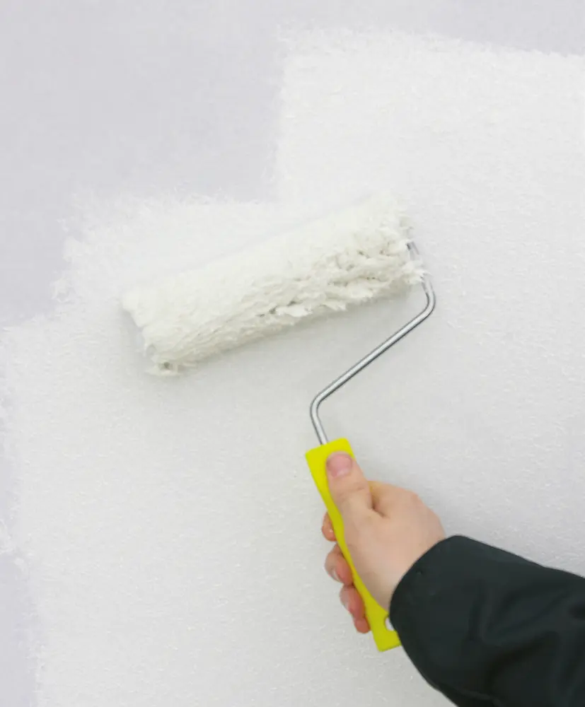 Målarroller med gult handtag används för att applicera vit färg på en vägg. Rollern har en mjuk yta för jämn täckning.