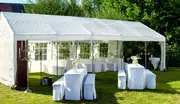 Stor hvid udendørs festtelt med vinduer, opstillet på græs. Inkluderer dækkede borde og bænke, blomsterdekorationer og dekorativ belysning, velegnet til arrangementer eller fester.
