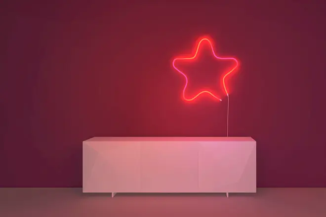 Moderne hvid skænk med geometrisk design, placeret mod mørkerød væg. Over den hænger en lysende neonlampe formet som en stjerne, der giver rummet et dekorativt præg.