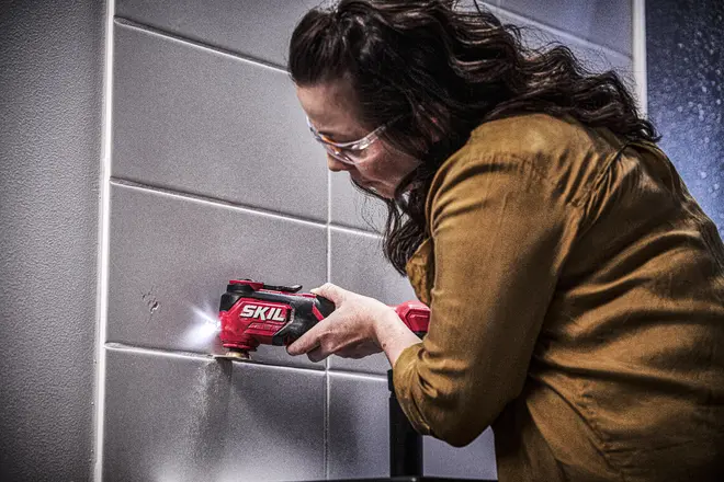 Rød SKIL trådløs roterende værktøj med LED-lys og ergonomisk greb, bruges til at skære eller slibe fliser. Kompakt, håndholdt design til præcisionsarbejde på hårde overflader.