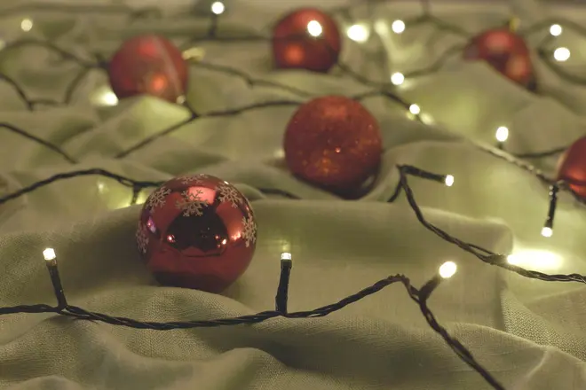 Røde glitrende julekugler og varme hvide lyskæder arrangeret på blødt grønt stof.