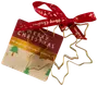 Juletræsformet metalornament med guldfinish, fastgjort til et festligt kort og rød bånd med guldbogstaver. Perfekt til juledekoration eller gave. Kortet har juletræer og hilsen.