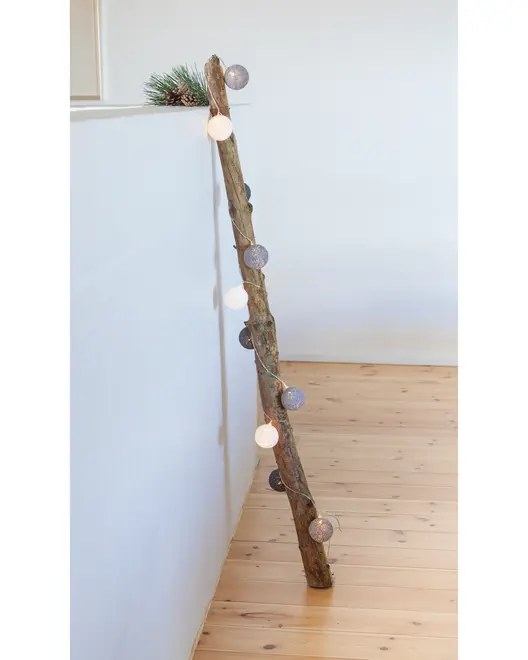 Dekorativ trästege med ljusslinga, runda vita och grå lampor. Rustik design, perfekt för heminredning eller festdekoration. Lutad mot vägg på trägolv.