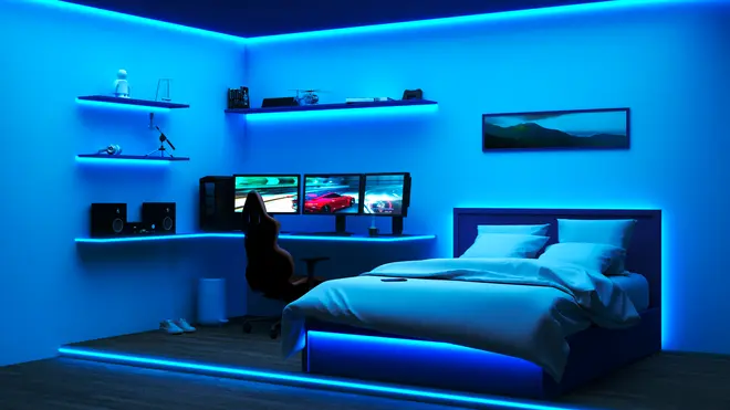 Moderne soveværelse med blå LED-belysning, gaming-setup med tre skærme, sort stol, hylder med dekoration, højttalere og en seng med hvidt sengetøj og oplyst sengegavl.