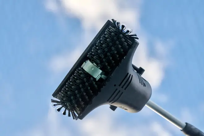 Rektangulært børstehoved med tætte sorte børster, monteret på teleskopstang. Velegnet til udendørs rengøring som vinduer eller solpaneler. Holdbar plast, synlig vandtilslutning.