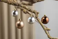 Fyra julgranskulor i metalliskt silver, guld och brons, blanka och matta, med guldfäste och snöre, upphängda på en gren.