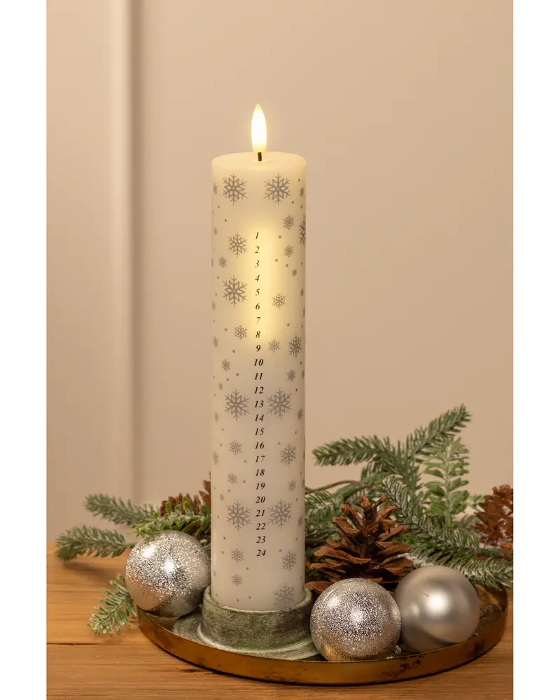 Högt vitt adventsljus med siffror 1-24 och silverfärgade snöflingor, på bricka med grankvistar, kottar och silvriga julkulor.